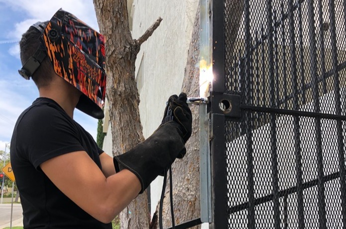 A locksmith welds a security plate on a metal gate to replace a lock.
